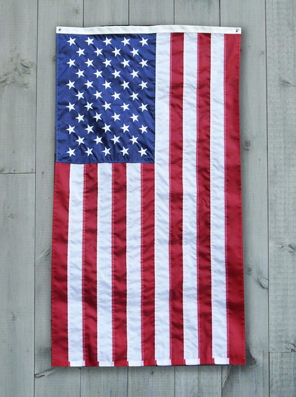 The flag of the United States of America hangs against a grey wood paneled wall.
